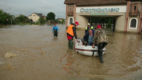 GALYCH, UKRAINE - JUNE 24, 2020: Flood survivors sitting in inflatable boat rescued by pair of rescuers. Family saved from flooded area or town. People natural disaster. Wait for evacuation mororboat