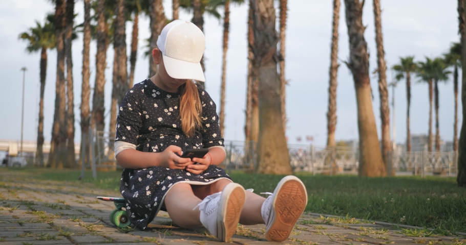 Girl riding on skateboard in tropical park. Active outdoor sport for kids.
