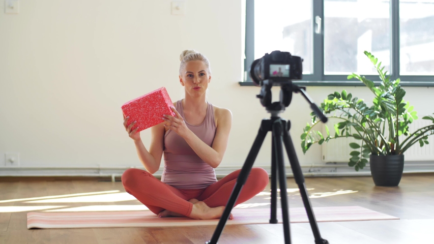 fitness, sport and video blogging concept - woman or blogger with camera on tripod and exercise block recording online yoga class in gym or studio - Powered by Shutterstock - Get 15% off with code: PIKWIZARD15