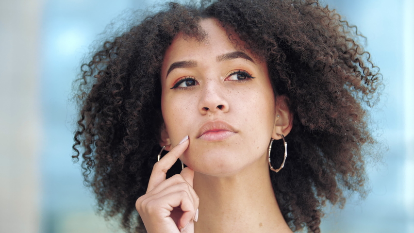 Young pensive afro american girl meditating thoughtfully at idea hold hand to chin, finger against cheekbone, with gesture of thought about problem solution with puzzled facial expression on street | Shutterstock HD Video #1056340694