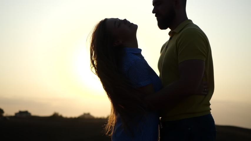 Silhouette of man and woman at sunset. Beautiful girl kisses guy in a deserted field, leaves and rises to hold her hands in slow motion. A romantic date and love on nature of loving happy couple Royalty-Free Stock Footage #1056340709