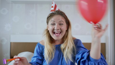 virtual communication, cheerful girl with balloons and hat congratulates her friend on her webcam happy birthday and celebrates an online party because of self-isolation on carnatine sitting at home