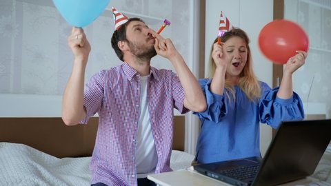 remote communication, funny man and woman in caps with horns and balls have fun, happy birthday to close friend via video communication on laptop using modern technology and celebrate an online