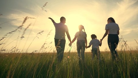 Happy family together. People hold hands on a walk on the green grass. The concept of teamwork. Happy father with daughters. Family walk on green grass. People holding hands walk across field in park
