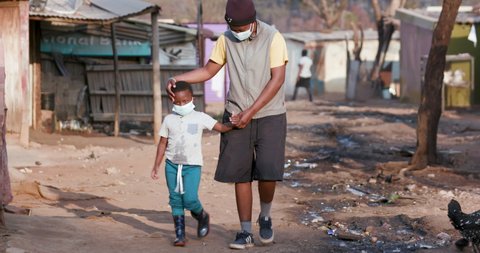 Poverty. Inequality.Black African mother and child walking in an informal settlement with protective face masks to prevent Covid-19