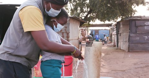 Close-up view of Black African mother demonstrating to her child how to wash his hands to prevent Covid-19 in an informal settlement