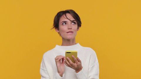 Smiling beautiful young woman girl 20s years old in white sweater posing isolated on yellow background in studio. People sincere emotions lifestyle concept. Look surprised hold using mobile cell phone
