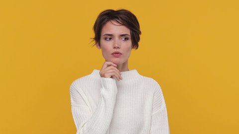 Pensive young woman 20s years old in white sweater posing looks around thinks scratches at temple comes up with ideas raised finger up isolated on yellow background in studio. People lifestyle concept