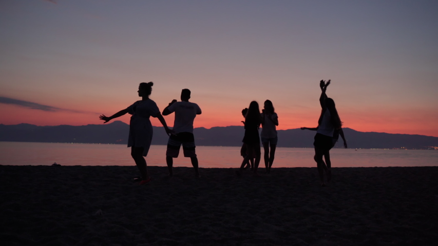 Beautiful sea sunset background, crowd of happy cheerful friends dancing barefoot at the sea beach. Silhouettes of dancing people lifting uptheir hands. Beach party background Royalty-Free Stock Footage #1056350006