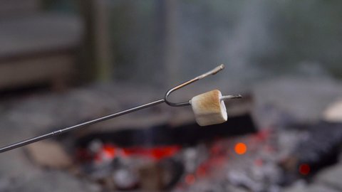 A person roasting a marshmallow with a campfire de-focused in the background. 