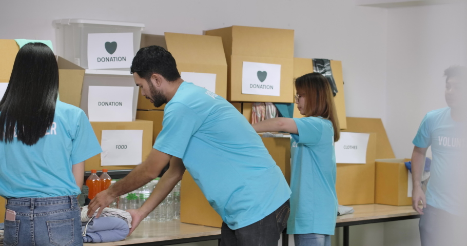 Young asian male and female volunteers sorting clothes in a donation box together as charity workers and members of the community work to the poor during the Coronavirus pandemic. Royalty-Free Stock Footage #1056350351