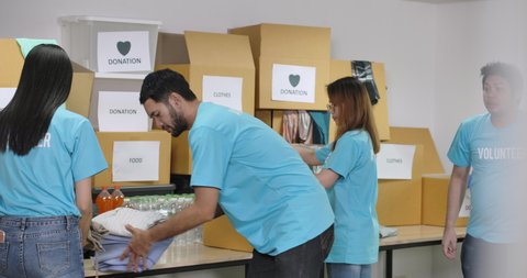 Young asian male and female volunteers sorting clothes in a donation box together as charity workers and members of the community work to the poor during the Coronavirus pandemic.