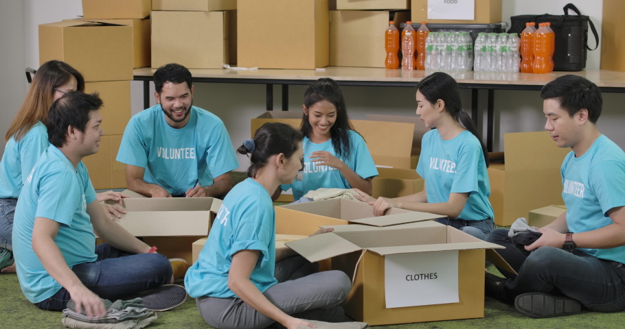 Young asian male and female volunteers sorting clothes in a donation box together as charity workers and members of the community work to the poor during the Coronavirus pandemic. Royalty-Free Stock Footage #1056350354