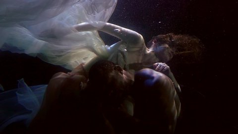 multiracial lovers underwater, man and woman are swimming inside dark deepness
