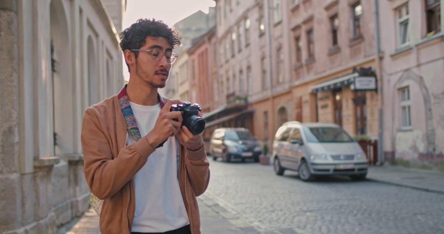 Millennial man with nose ring taking photo on camera of city scape. Good looking male tourist in glasses standing at old city street. Concept of travelling, tourism and photography.