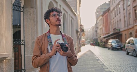 Millennial man with nose ring taking photo on camera of city scape. Good looking male tourist in glasses standing at old city street. Concept of travelling, tourism and photography.