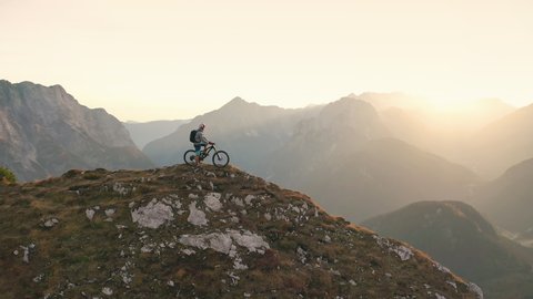 Aerial - A male mountain biker enjoying the view of the beautiful mountains in the background at sunset. 4K
