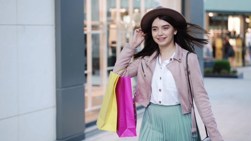 Young smiling woman in hat with paper bags walking in the shopping center after quarantine. | Shutterstock HD Video #1056356807