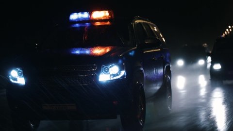 Police SUV driving at high speed in the rain at night. Flashers. The car splashes water from puddles with its wheels.