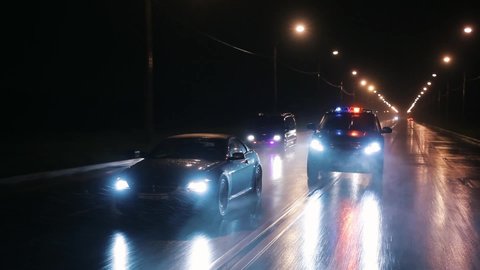 Cop cars are chasing an intruder's car in the rain. Outdoor front view of police traffic auto driving. Shot on the Russian Arm.