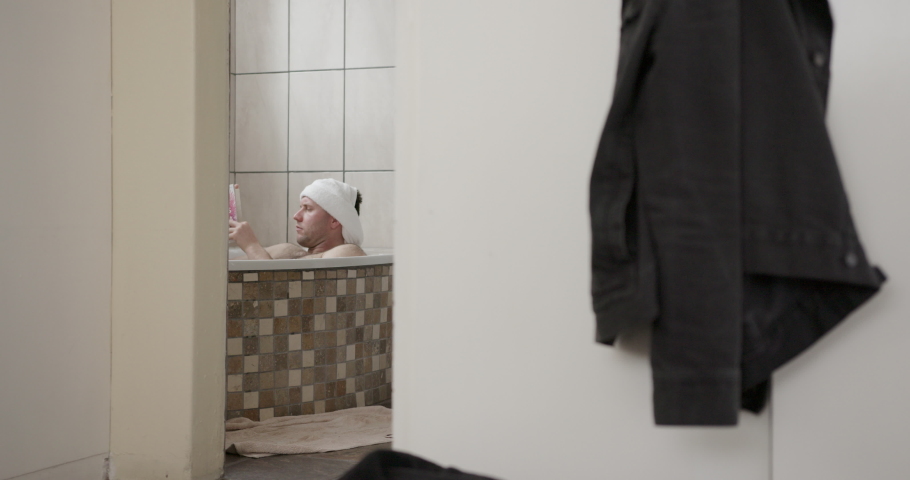 Young man sitting in bathtub and reading book