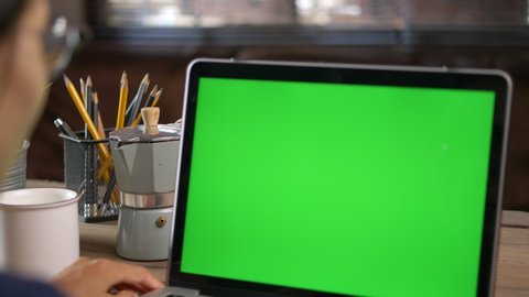 ​4K Dolly short. Over the shoulder shot of a business woman working in office interior on pc on desk, looking at green screen. Office person using laptop computer with laptop green screen,