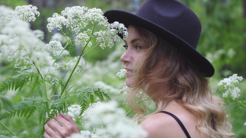 Young pretty woman in hat poses in deep forest among white flowers.