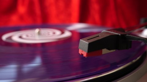 Stylus arm and needle lowered on 12” purple vinyl record on a DJ turntable on red velvet background. Retro LP platter. Close up. Hi-fi. Disco, punk, grunge, pop. 60s, 70s, 80s, 90s 4K