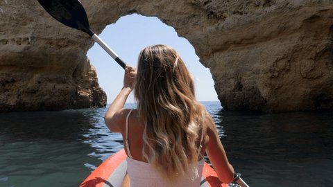 Rear view of woman paddling on red canoe in Portugal going trough rocky caves and cliffs. Slow motion video 