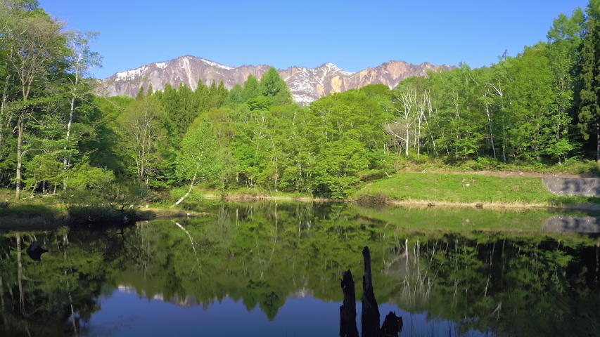 Wide angle aerial view footage of a scenic landscape with a lake, forest and a mountain range, Amaike Pond, Akiyamago, Niigata Prefecture, Japan