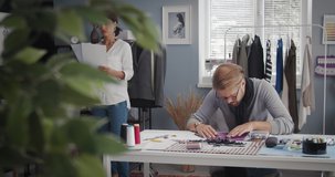 Professional male and female designers consulting with with other about sketches at modern atelier. Two fashion people coworking on new clothing collection.