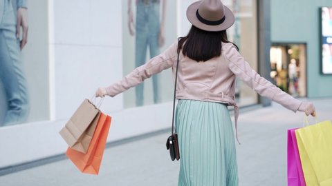 Young attractive woman walks with colorful shopping bags around shopping mall after quarantine. Back view.