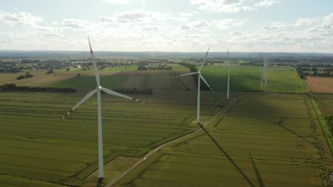 Drone shot on energy production of wind turbines at sunset. Wind Power Turbines Generating Clean Renewable Energy for Sustainable. Aerial view of a wheat field with windmills.