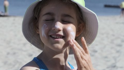Mother Applying Sunblock Cream on Kid. Mom Applying Sunscreen Lotion on Daughter at Beach. Mother Preparing Child for Bath in Sea. Happy Family at Beach Sun Protection. Travel Summer Suntan Vacation.