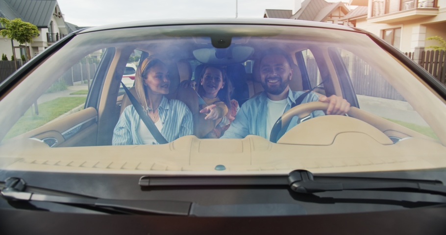 Front view of happy bearded man driving, happy woman with short hair sitting in passenger seat chatting with little girls sitting in back. Concept of lifestyle, happy family, travel together. Royalty-Free Stock Footage #1056379154