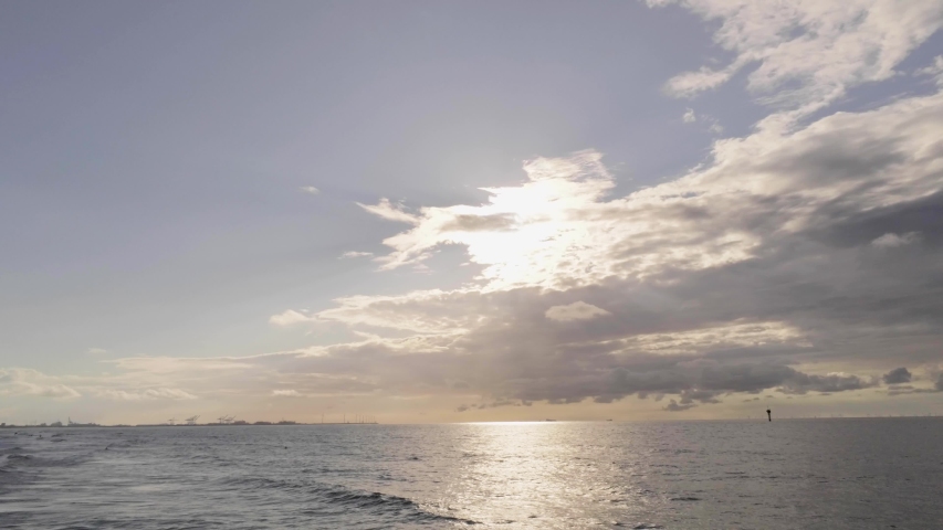 Golden sun filtering through high clouds as a seagull crosses and returns, North Sea, Belgium, aerial
