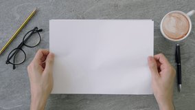 Top view shot of a man holding a stack of a4 sheets of paper above on a marble table top surface with coffee, reading glasses and office utensils. - Powered by Shutterstock - Get 15% off with code: PIKWIZARD15