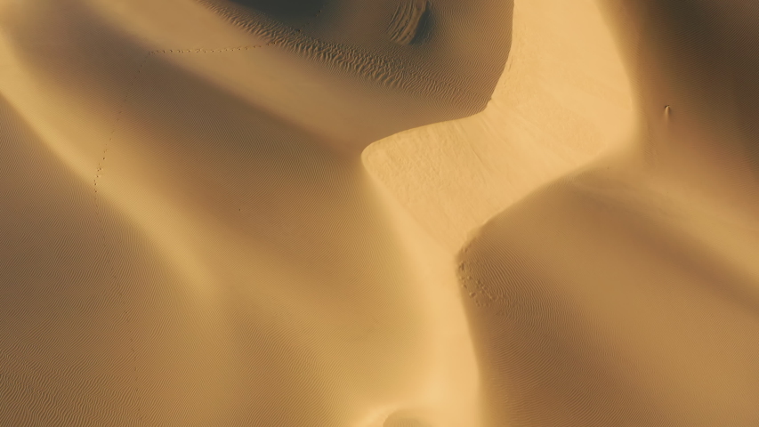 4K top down view on the abstract wavy pattern on the sand desert surface painted by the sunset light and deep shadows on the high dunes. Beautiful aerial background of the wild nature scenic landscape Royalty-Free Stock Footage #1056386201