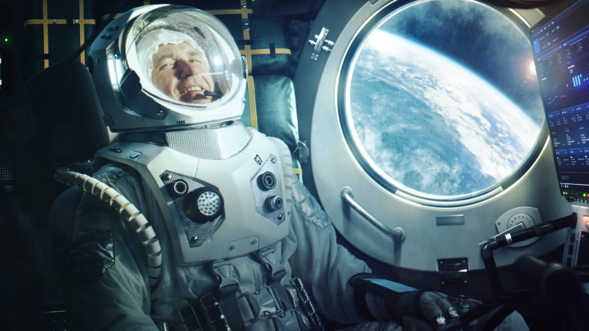 Portrait of a Happy Astronaut on a Space Ship In Orbit. Cosmonaut in a Futuristic Suit is Full of Joy and is Waving Hand on a Video Call. VFX Graphics Footage from the International Space Station. Royalty-Free Stock Footage #1056387902