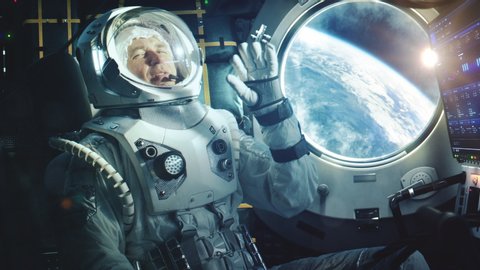 Portrait of a Happy Astronaut on a Space Ship In Orbit. Cosmonaut in a Futuristic Suit is Full of Joy and is Waving Hand on a Video Call. VFX Graphics Footage from the International Space Station.