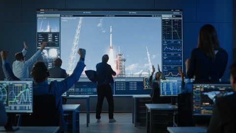 Group of People in Mission Control Center Witness Successful Space Rocket Launch. Flight Director is Pacing Nervously in Front of the Screen and Punches the Air in Celebration. Team Claps Hands.