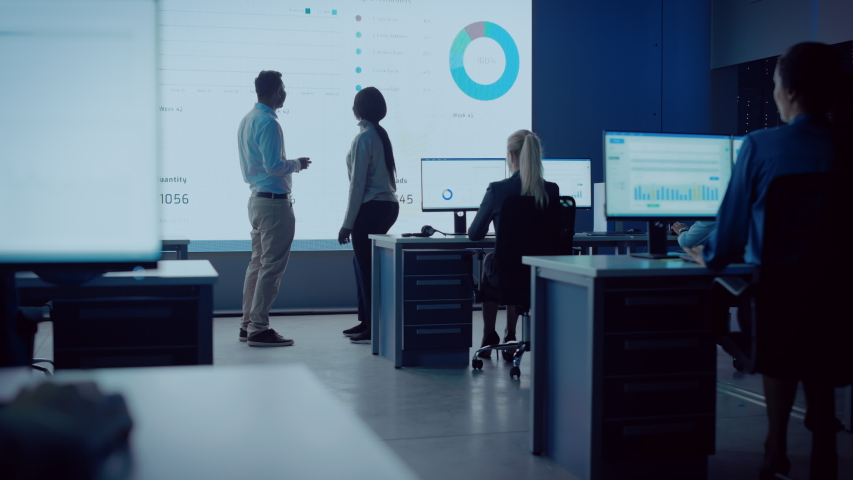 Two Financial Data Analysts Having a Meeting in a Modern Monitoring Office with Analytics Feed on a Big Digital Screen. Monitoring Room with Brokers and Finance Specialists Sit in Front of Computers. | Shutterstock HD Video #1056388001
