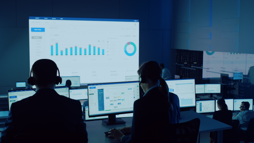 Professional Financial Data Analysts Working in a Modern Monitoring Office with Live Analytics Feed on a Big Digital Screen. Monitoring Room with Finance Specialists Sit in Front of Computers.  | Shutterstock HD Video #1056388019