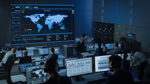 Static Shot of Officers in a Surveillance Control Center with Police Global Map Tracking on a Big Digital Screen. Monitoring Room Employees Sit in Front of Computer Displays and Analyze Big Data.