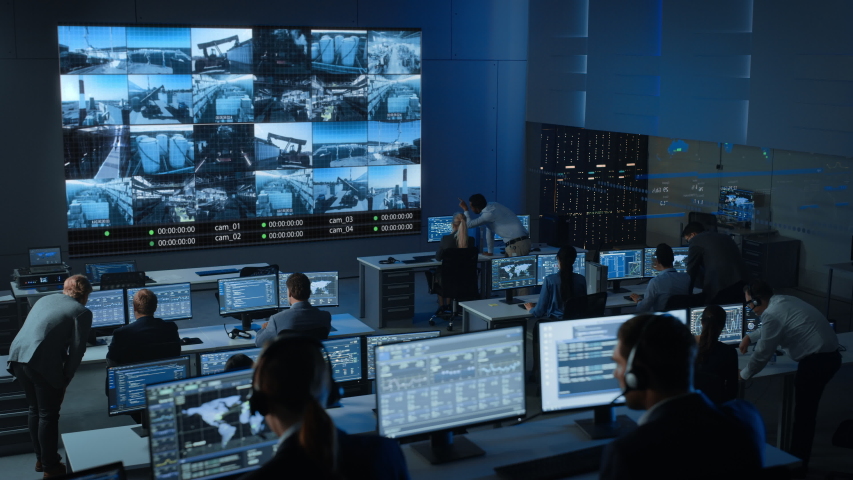 Static Shot of a Group of Professionals Working in a Surveillance Center with CCTV Video Footage from an Industrial Factory on a Big Digital Screen. Monitoring Room Employees Sit in Front of Computers | Shutterstock HD Video #1056388097
