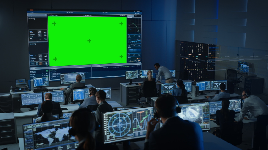 Big Green Screen Horizontal Mock Up in a Mission Control Center Room with Flight Director and Other Controllers Working on Computers. Team of Engineers Work in Monitoring Room Full of Displays. Royalty-Free Stock Footage #1056388103