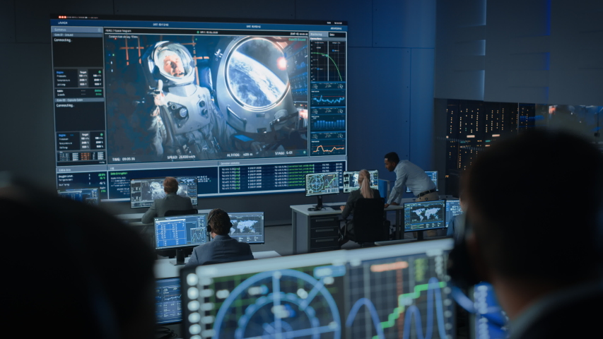 Group of People in Mission Control Center Establish Successful Video Connection on a Big Screen with an Astronaut on Board of a Space Station. Flight Control Scientists Sit in Front of Computers. | Shutterstock HD Video #1056388127