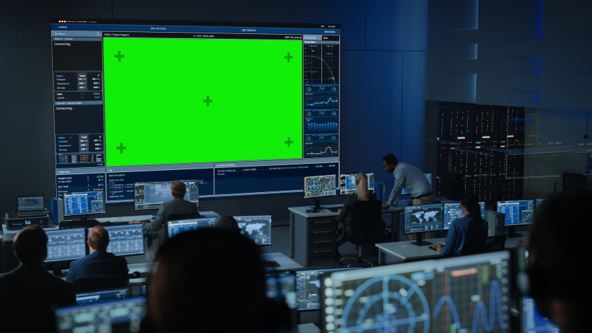 Big Green Screen Horizontal Mock Up in a Mission Control Center Room with Flight Director and Other Controllers Working on Computers. Team of Engineers Work in Monitoring Room Full of Displays. Royalty-Free Stock Footage #1056388133