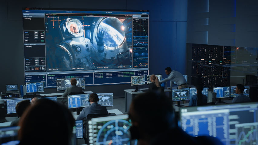 Group of People in Mission Control Center Establish Successful Video Connection on a Big Screen with an Astronaut on Board of a Space Station. Flight Control Scientists Sit in Front of Computers. | Shutterstock HD Video #1056388139