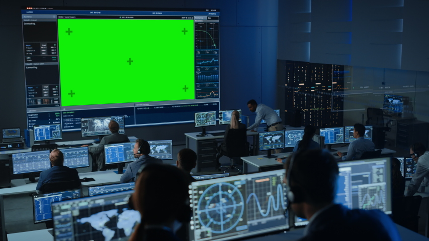 Big Green Screen Horizontal Mock Up in a Mission Control Center Room with Flight Director and Other Controllers Working on Computers. Team of Engineers Work in Monitoring Room Full of Displays. | Shutterstock HD Video #1056388148